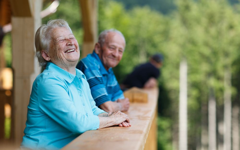 Happy senior couple looking to surroundings areas and smiling. Posing in wooden tower and watching for nature scenery in forest. Blurred forest background.