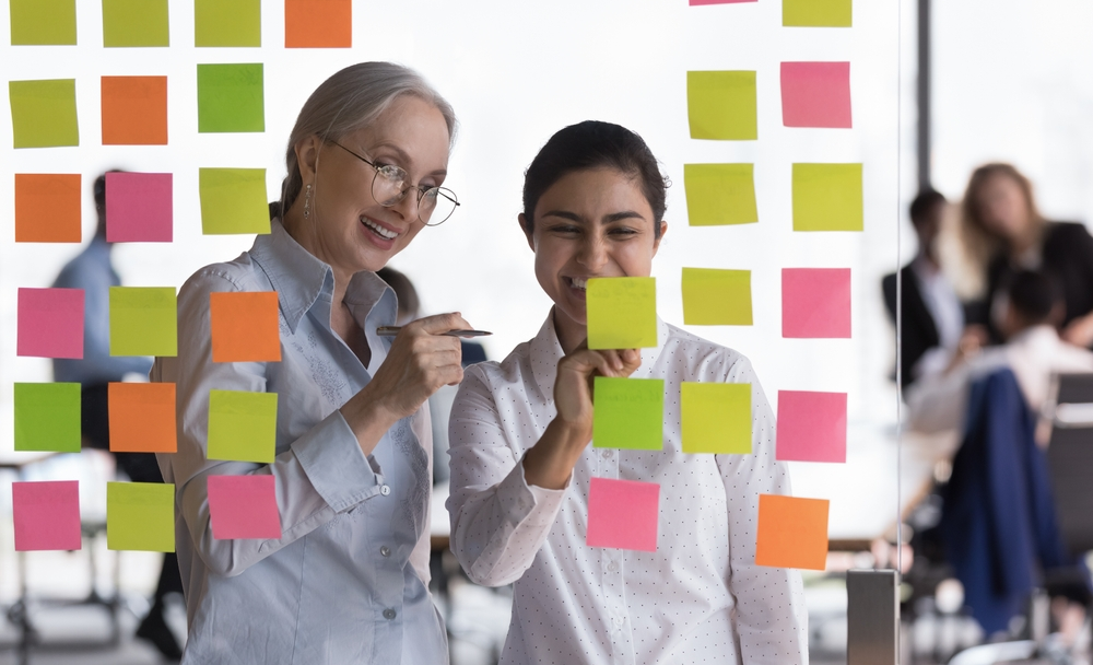 Older adult and young adult female looking at post-it notes in discussion in